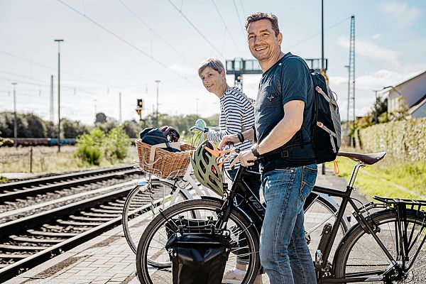 Zwei Personen warten mit ihren Fahrrädern am Bahnsteig 