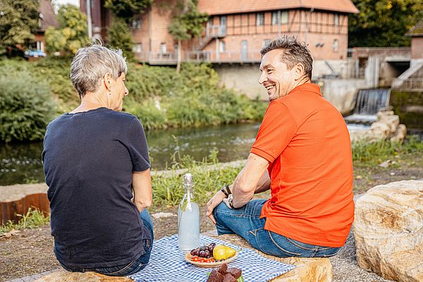 Zwei Personen machen eine Picknickpause an einem Fluss 